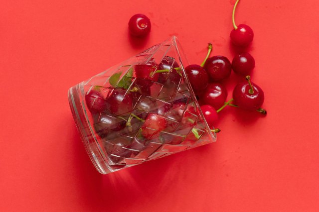An image of cherries spilling out of a glass against a red background