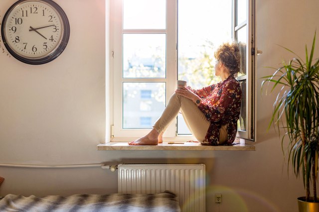An image of a woman sitting on a window sill looking outside