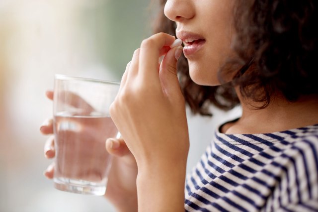 An image of a woman taking a pill with a glass of water