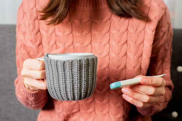 An image of a woman in a coral sweater holding a mug with a grey koozie and a thermometer 