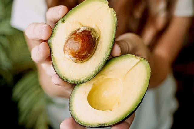 A person holds an avocado that has been sliced in half