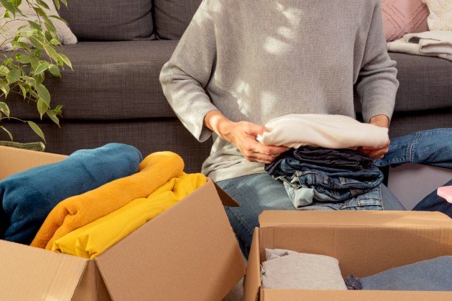 An image of a woman sitting of the floor and putting clothes in cardboard boxes