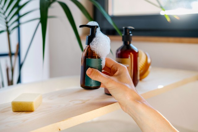 An image of a hand pulling a bottle of soap off a bathtub shelf