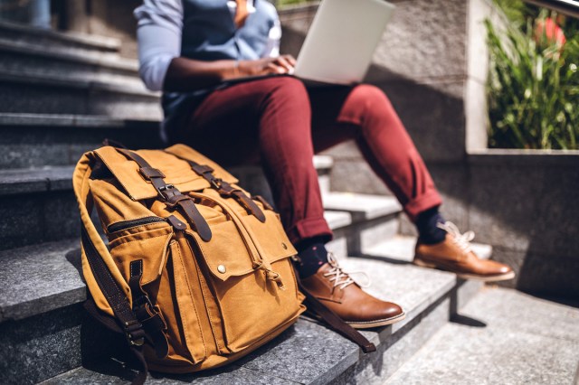 An image of a man sitting on steps with a laptop and backpack