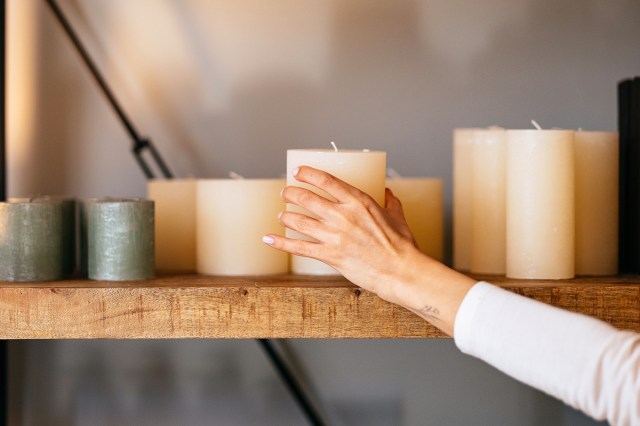 An image of a person holding a cream candle on a shelves of candles