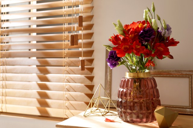 An image of a vase of flowers on a table next to wooden blinds