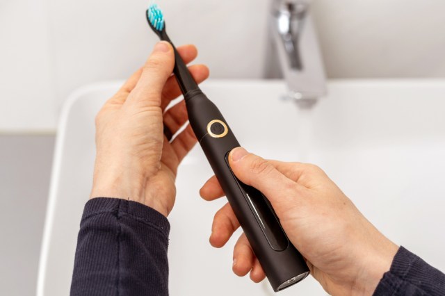 An image of hands holding a black electric toothbrush