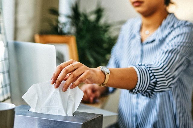 An image of a woman pulling a tissue out of a tissue box