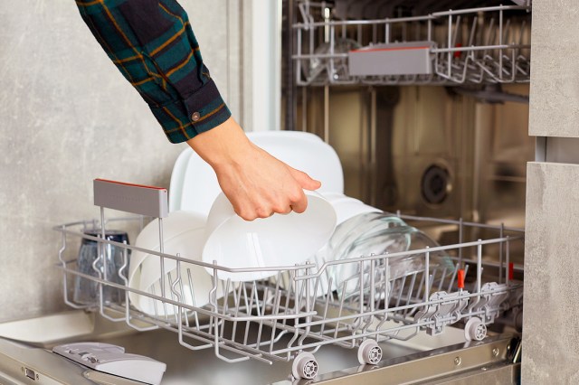 A hand places a dish in the bottom rack of the dishwasher
