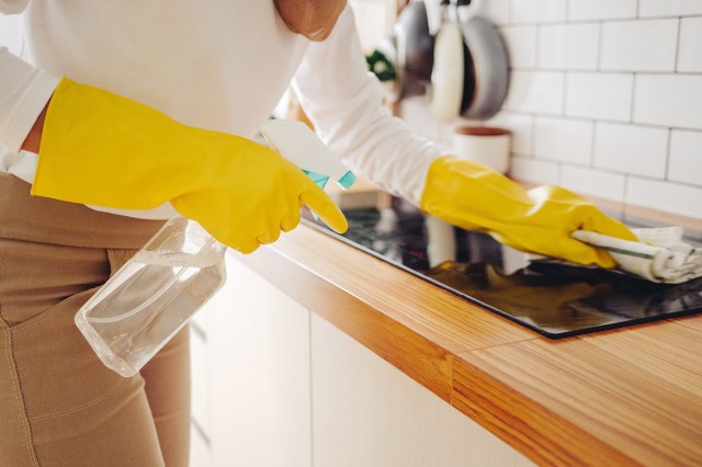 An image of a woman wearing yellow rubbing gloves scrubbing a stove