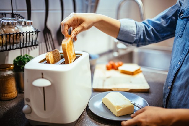 An image of a person taking toast out of a white toaster