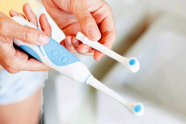 An image a person holding an electric toothbrush and a toothbrush head