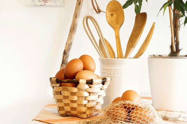 Eggs in a basket next to a container of wooden utensils