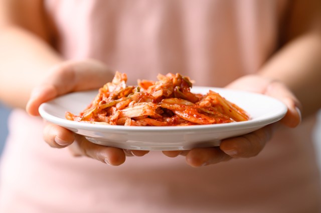 An image of a hands holding a plate of kimchi
