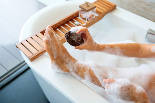 An image of a person in a bathtub scrubbing their foot with a pumice stone