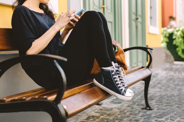 An image of a woman wearing black and white sneakers sitting on a bench outside