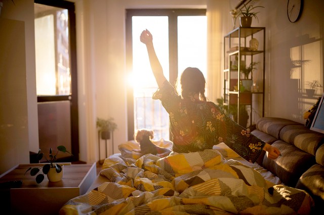 An image of a woman sitting on a bed stretching at sunrise