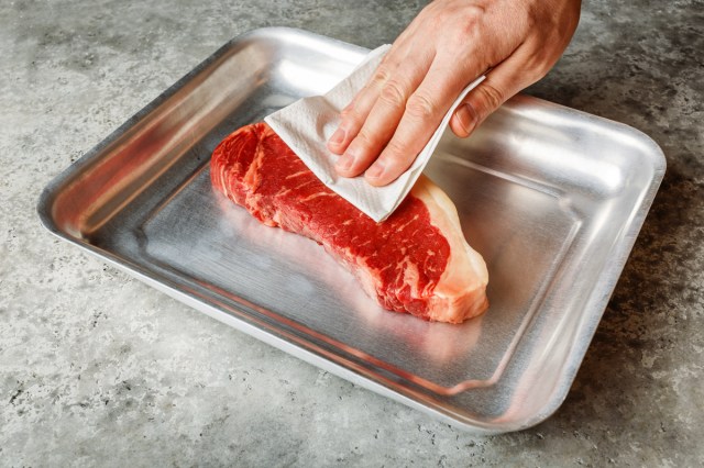 An image of a person patting a steak dry