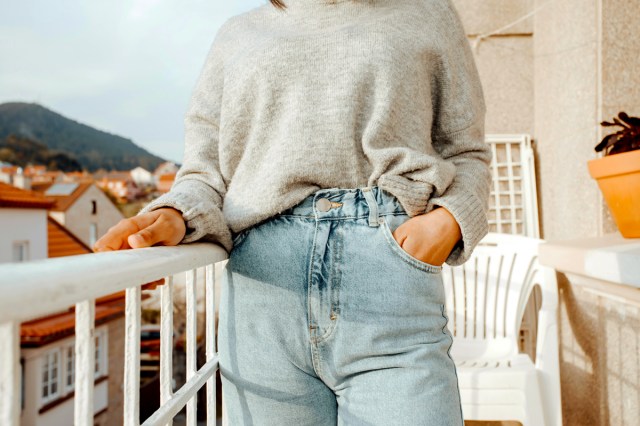 An image of a woman standing on a balcony with her hand in her jeans pocket