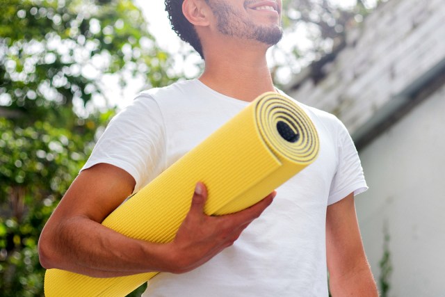 An image of a man holding a yellow yoga mat