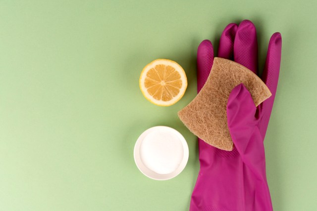 An image of a pink rubber glove holding a sponge next to a lemon half and a white bowl of baking soda