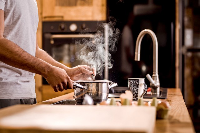 A person stirs a steaming pot nearby a sink