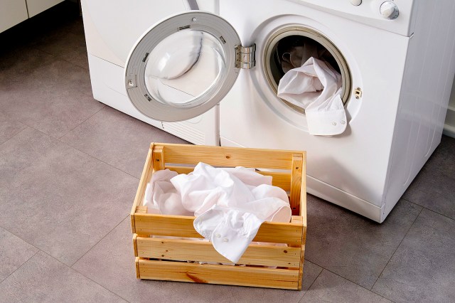 An image of an open dryer with clothes in it next to a wooden crate with a white shirt in it
