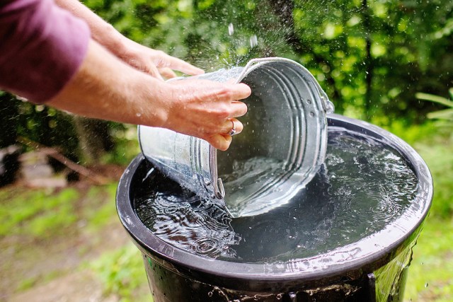 A man uses a bucket to scoop water from a large container