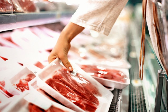 An image of a person grabbing a package of meat from a grocery store shelf