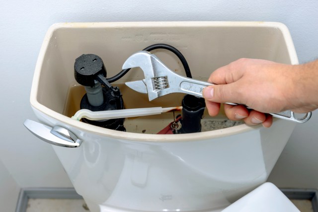 An image of a person holding a wrench over a toilet without the lid