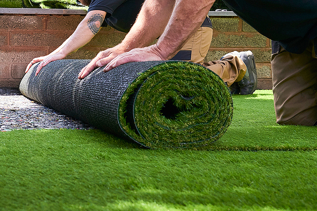 Two people lay down a sheet of lawn grass