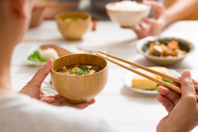 An image of a person holding a bowl of soup with chopsticks