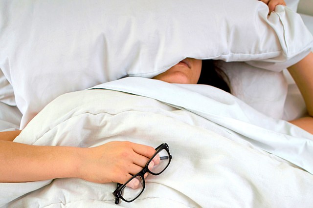 An image of a woman in bed with a pillow over he head