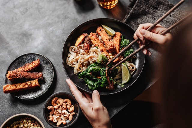 An image of a person holding chopsticks into a bowl of Asian food