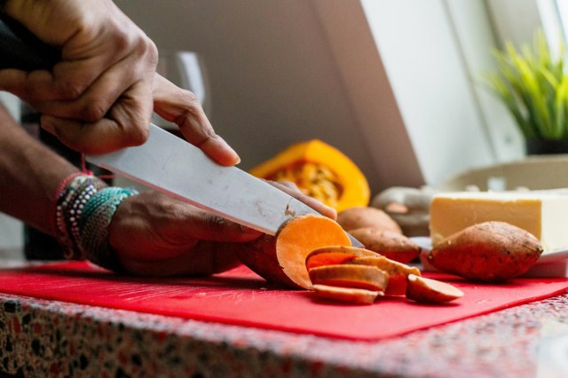 A person cuts a sweet potato on a red cutting board