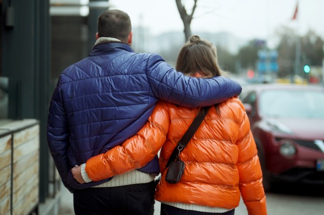 An image of a man and a woman in puffer coats with their arms around each other