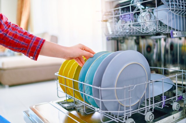 A person in a red plaid shirt loads the dishwasher