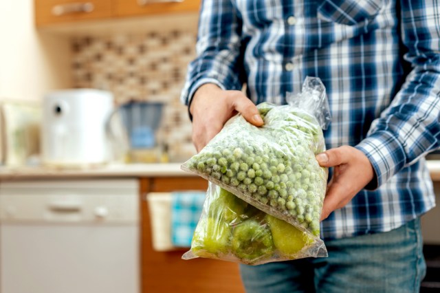 A person holds two clear plastic bags full of frozen vegetables