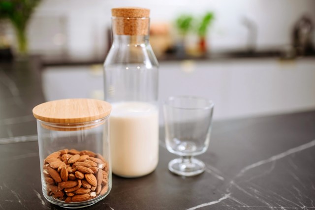 An image of a jar of almonds, a bottle of milk, and a glass on the counter