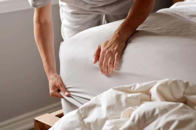 An image of a man putting a white fitted sheet on a bed