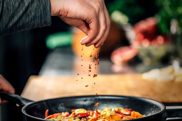 An image of a person sprinkling spices into a pan of food