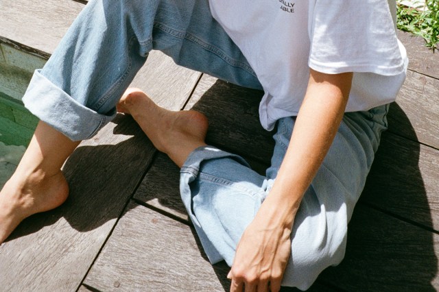 An image of a person wearing a white t-shirt and blue jeans sitting on a dock
