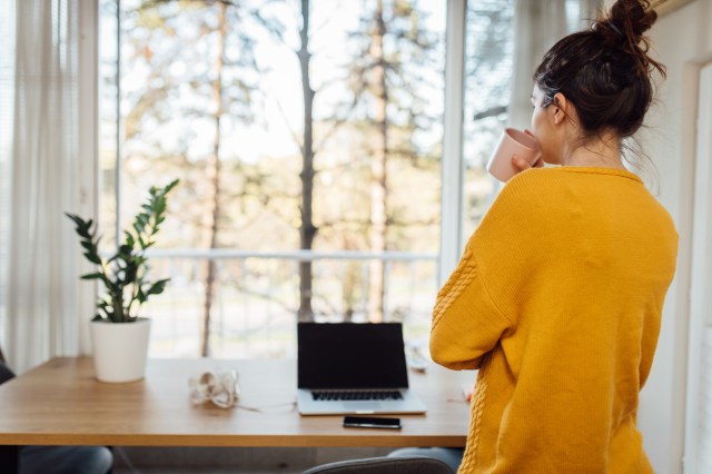 An image of a woman drinking out of a cup in front of a desk and window