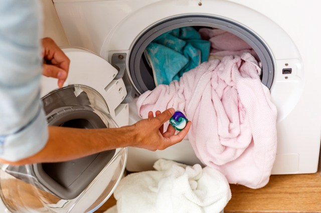 An image of a person putting a laundry pod into a washing machine filled with clothes