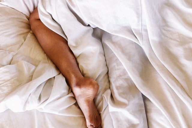 A close-up image of a person lying in a bed with white sheets