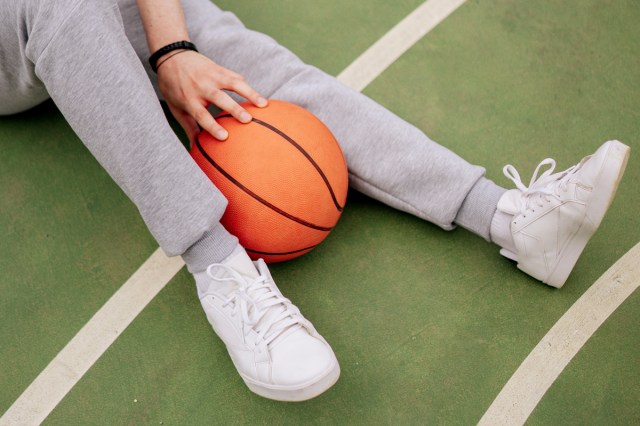An image of a person sitting on a basketball court with a basketball between their legs