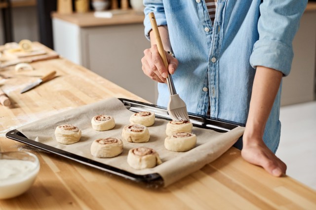 An image of a woman brushing the top of cinnamon rolls on a baking sheet