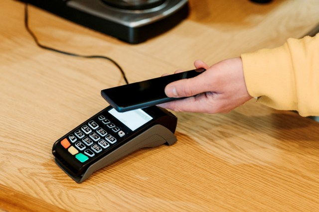 An image of a person holding their pone to a credit card machine