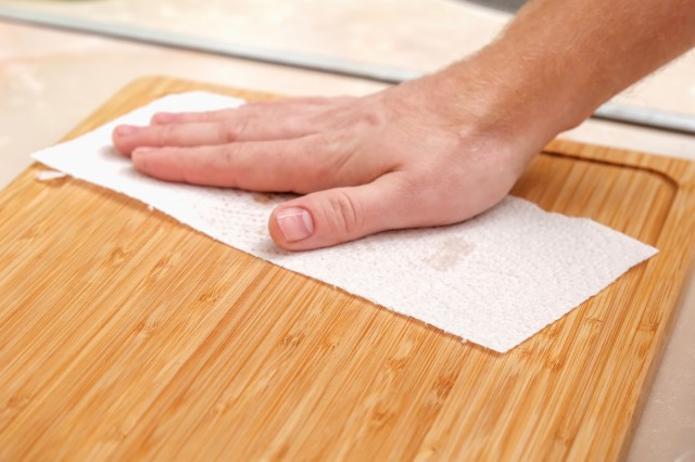 An image of a hand wiping a wooden cutting board with a paper towel