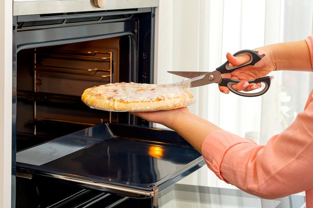 An image of a person cutting the plastic off a frozen pizza